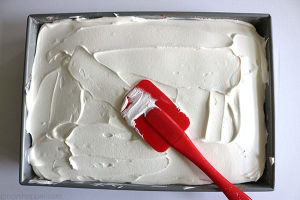 Adding Cool-Whip to strawberry poke cake.