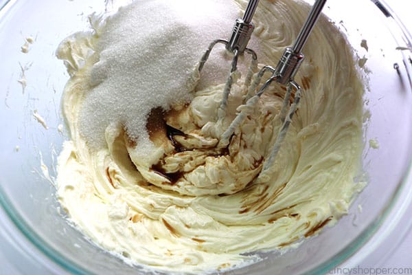 Adding sugar and vanilla to cheesecake mixture.