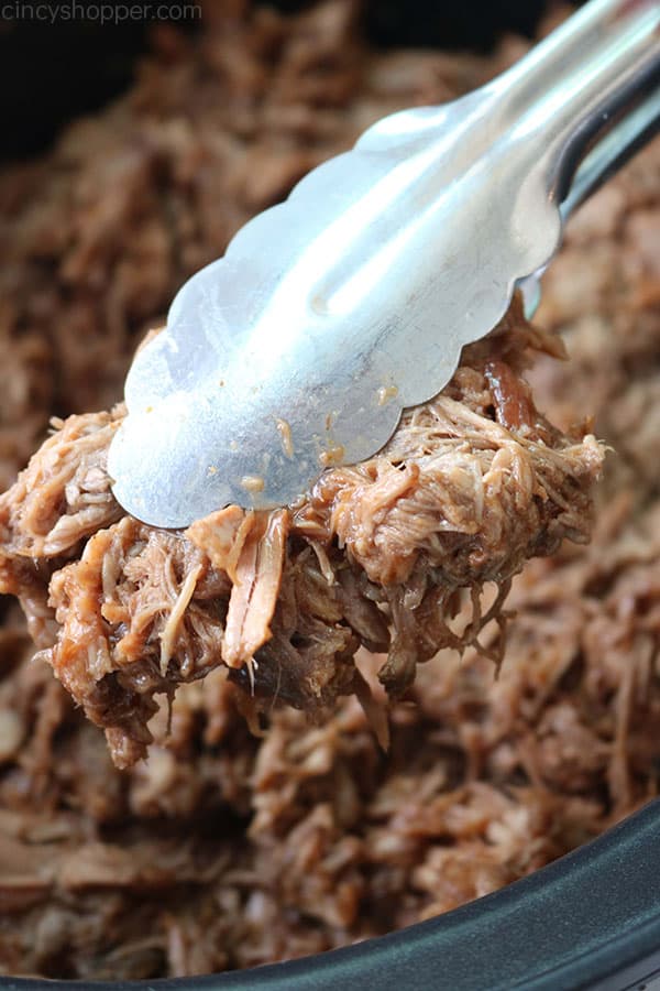 Dr. Pepper Pulled Pork in a Crock Pot with tongs.