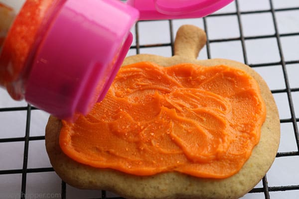 Adding sugar to pumpkin shaped cookies.
