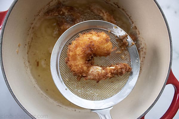coconut fried shrimp being removed from a pot of oil
