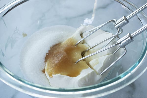 electric mixer beating cream cheese and sugar together in a glass bowl