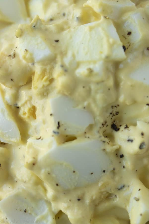 close up image of hard boiled eggs mixed with mayo, yellow mustard, salt, and pepper