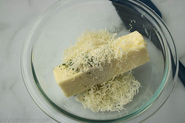 soft stick of butter in a bowl with shredded Parmesan cheese and spices