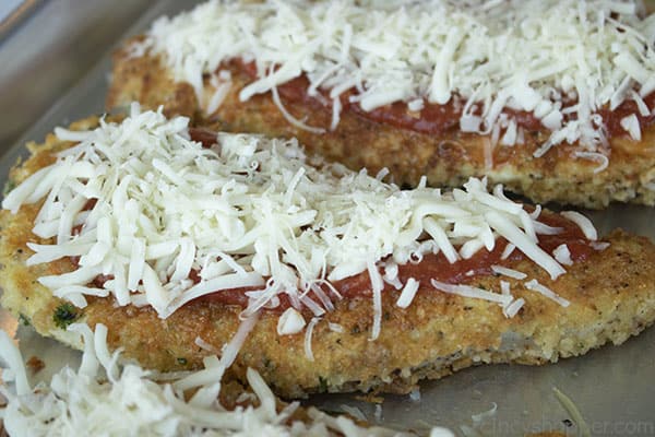 topping chicken Parmesan with shredded Mozzarella cheese