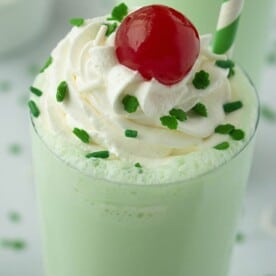 tall glass with thick green mint milkshake, whipped cream and cherry on top