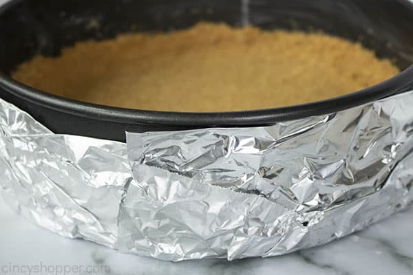 springform pan with graham cracker crust inside, wrapped in tin foil