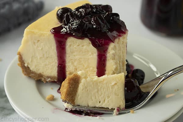 slice of creamy baked cheesecake on a plate covered in blueberry sauce