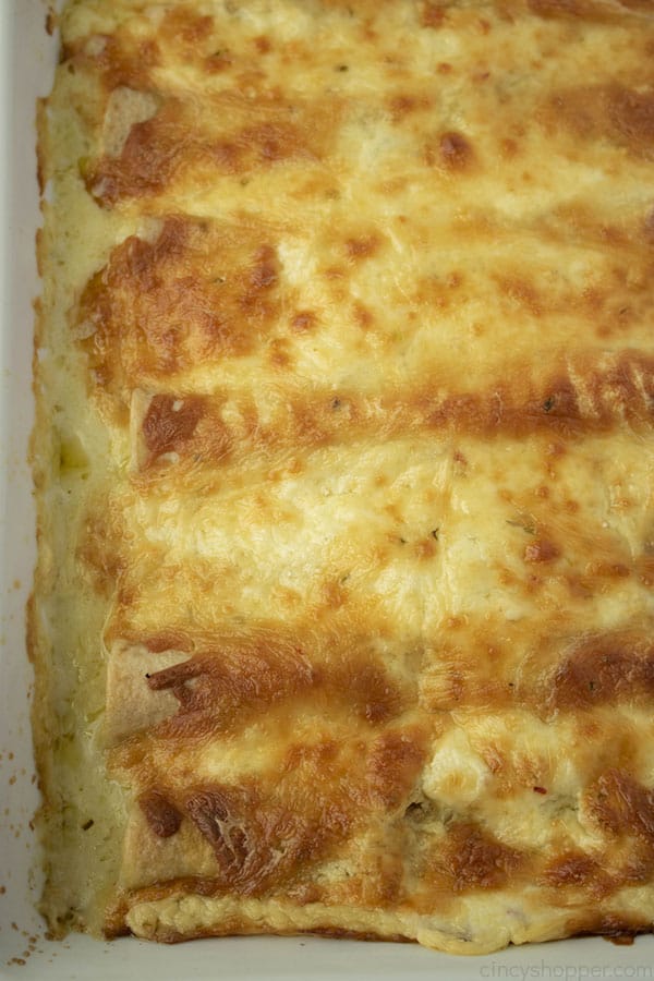 close up image of baked chicken enchiladas in casserole dish