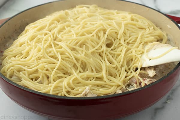 adding cooked spaghetti noodles into a skillet dinner