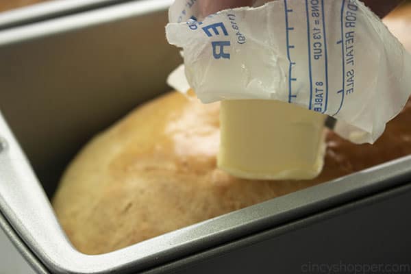 buttering the top of a homemade loaf of bread