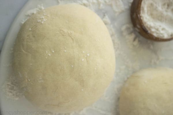 Pizza dough balls on a floured surface.