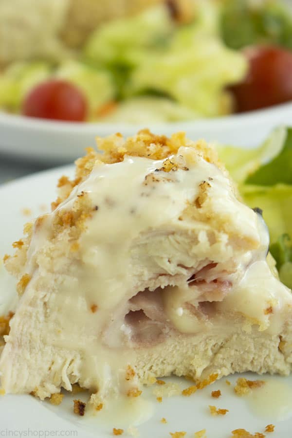 plate of stuffed chicken and sauce with a bowl of salad in the background