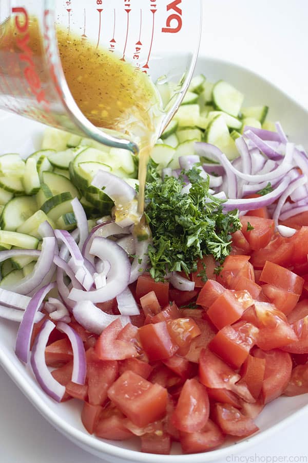 vinaigrette being poured from a measuring cup over chopped vegetables