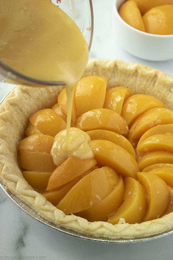 Pouring custard mixture over peaches in a pie crust