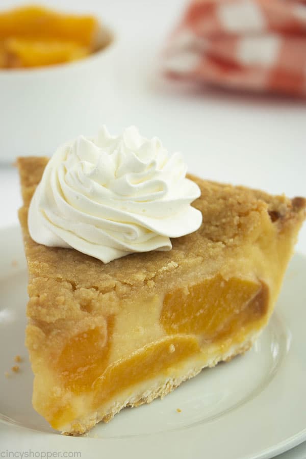 Slice of peach custard pie on a white plate with whipped topping