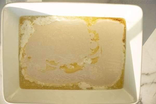 Cobbler batter on the top of melted butter in a white baking dish.