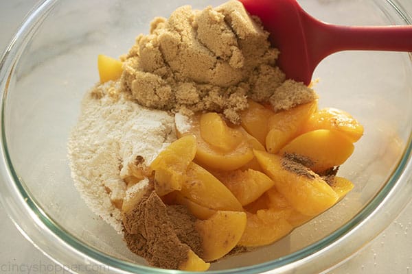 Sugar, flour, cinnamon, nutmeg and peaches in a mixing bowl