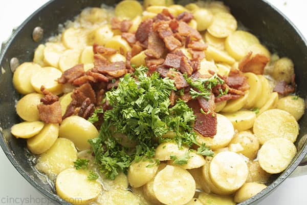 Cooked potatoes and onion in a skillet topped with cooked bacon and chopped parsley