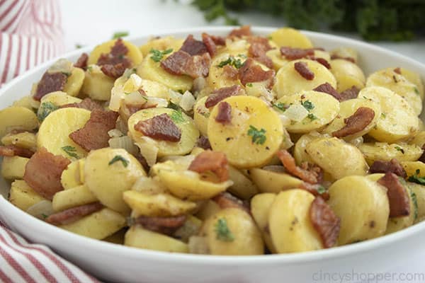 Bowl of warm potato salad with bacon with a striped dish towel 