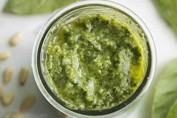 jar of pesto on a counter surrounded by fresh basil and pine nuts