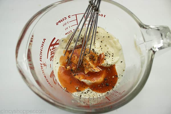 Metal whisk in a measuring cup with pasta salad dressing ingredients