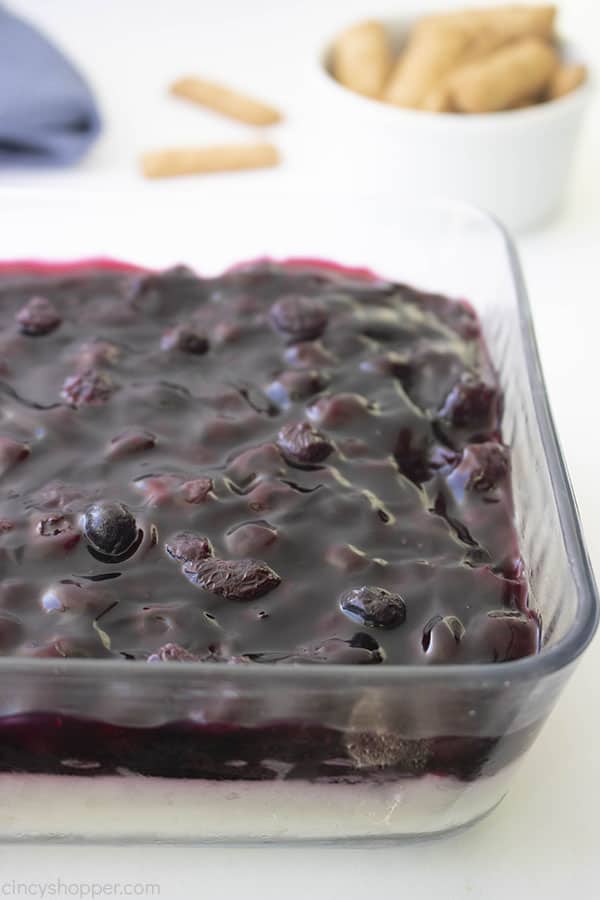 Layered Blueberry Cheesecake Dip in a clear dish on white background with graham crackers in background