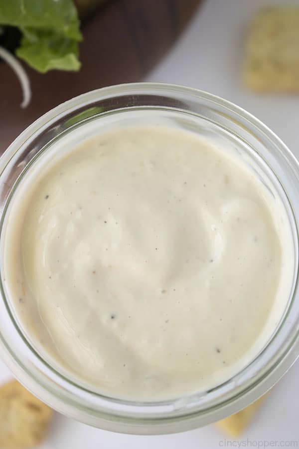 Overhead Caesar dressing in a clear jar with a white background with croutons scattered