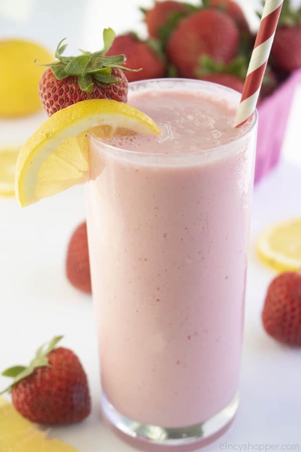 Frosted Strawberry Lemonade in a tall clear glass with straw, berries and lemon slice.