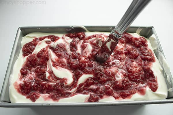 Layered raspberry cheesecake ice cream in a loaf pan with knife to make swirls