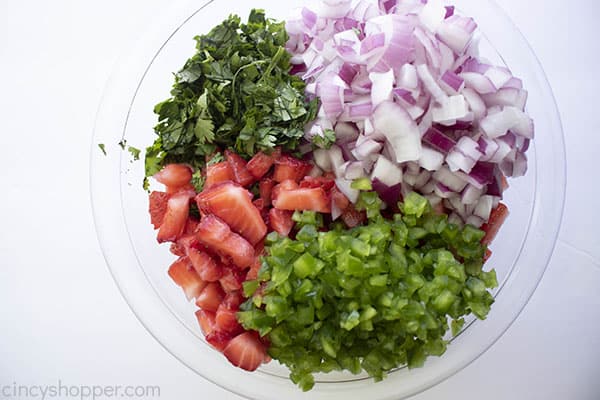 Diced and chopped ingredients for fruit salsa laid next to each other in clear mixing bowl