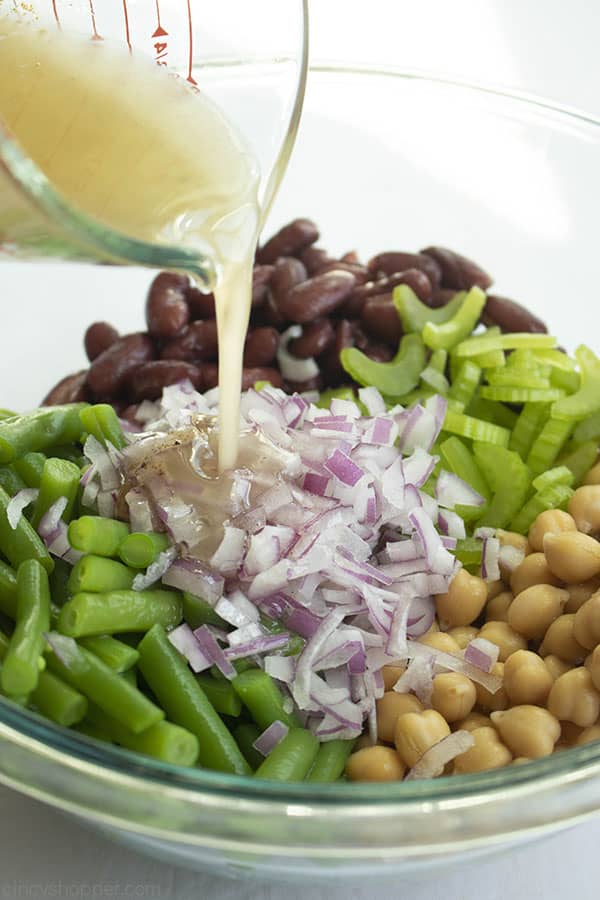 Dressing being poured from a measuring cup over bean salad ingredients