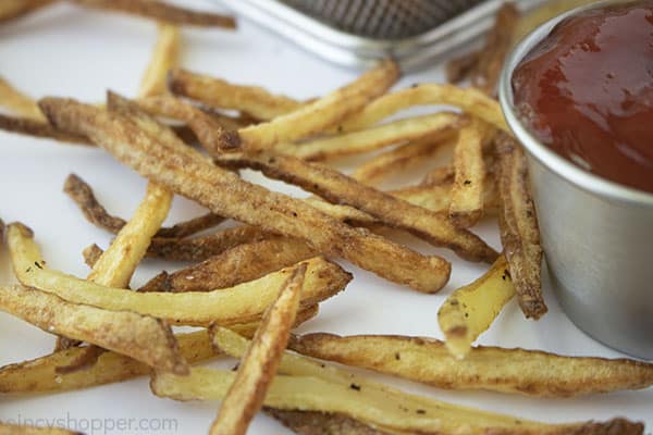 Crispy fries on a white background with ketchup in a small stainless dish