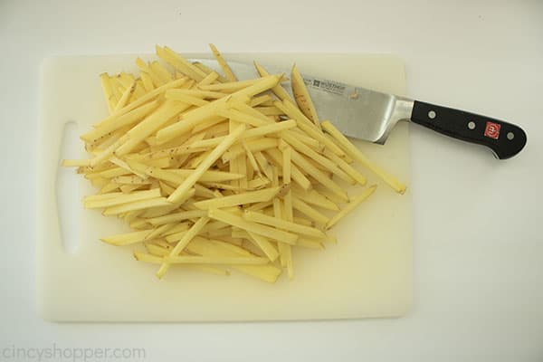 Skinny sliced raw potatoes on a white cutting board with a knife