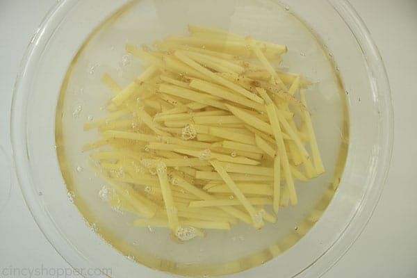 Raw fries in a clear bowl with water and a whit ebackground