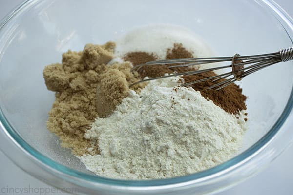 dry ingredients for the crisp topping in a large clear mixing bowl and an whisk on the right side of the bowl 