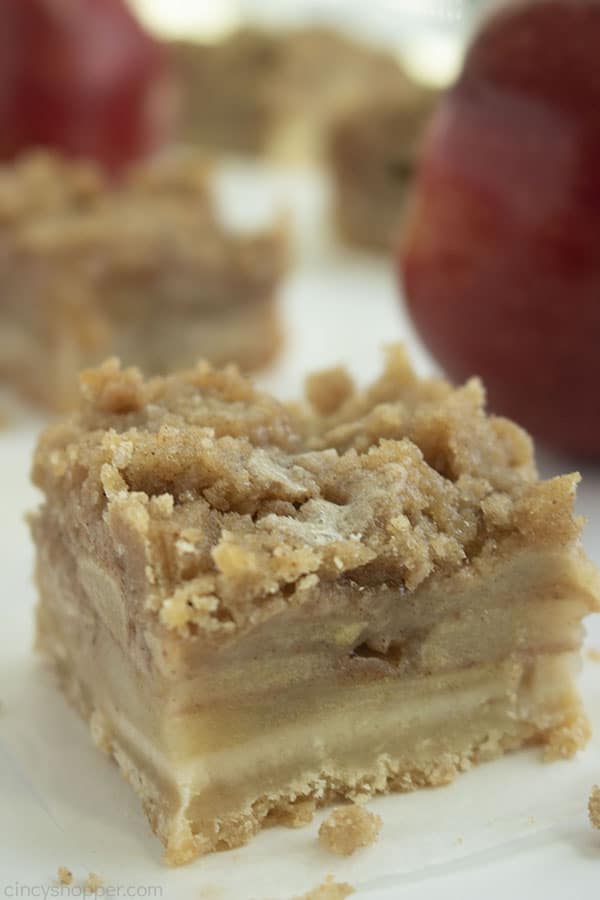 close up of an apple crisp bar on white paper with 2 apples in the background 