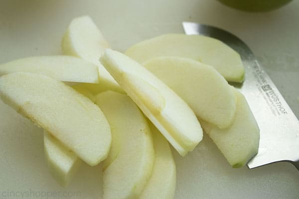 peeled green apple slices on a white cutting board with a large knife on the right side