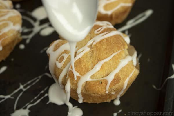 Spoon with icing drizzling on top of baked apple pie bites.