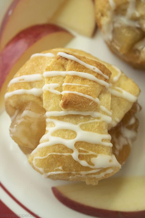 Mini apple pies made with crescent rolls on a white plate with red banding includes apple slices.