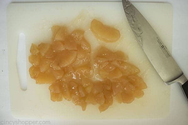 Diced apple pie filling on a white cutting board with knife.