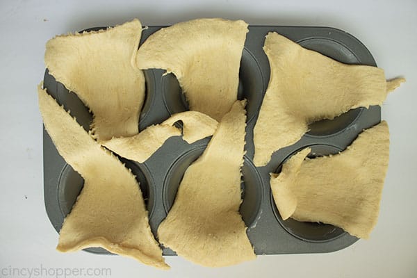 Crescent rolls draped over dark muffin pan.