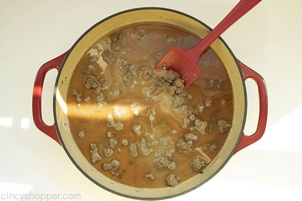 Overhead image of the Hamburger Helper Beef with the dry mixture added to it in a red cast iron skillet with a red spatula 