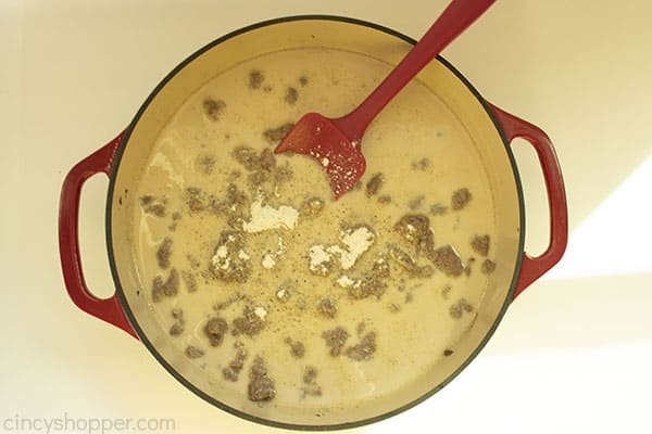 Overhead image of the Hamburger Helper Beef with the dry mixture added to it in a red cast iron skillet with a red spatula 