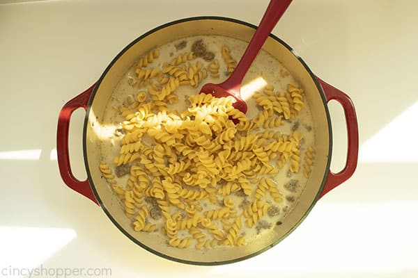 Overhead shot with the pasta added to the Hamburger Helper Mixture in a red cast iron skillet and a red spatula 