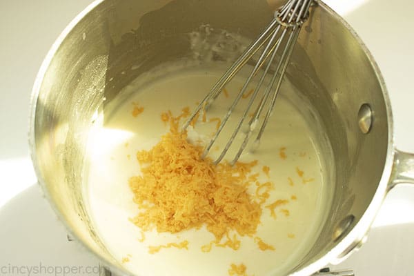Image of the Cheese being added to the Cheese Mixture in a medium saucepan 