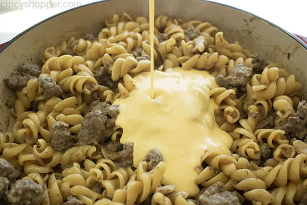 Image of the Macaroni Hamburger Helper with the Cheese Sauce being poured over in a large cast iron skillet 