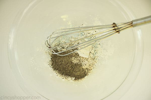 Dry ingredient mixture for the Macaroni Hamburger Helper in a large clear mixing bowl with a sliver whisk