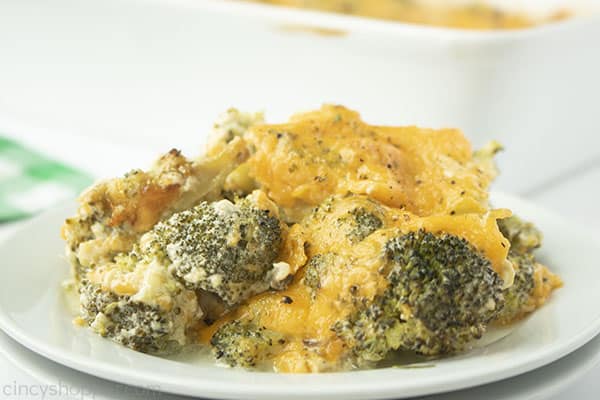 Cheesy Broccoli Casserole serving on a white plate with a green napkin and casserole dish in background