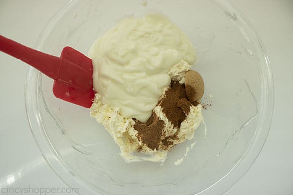 Overhead shot of more ingredients being added into the larger clear bowl with a red spatula 